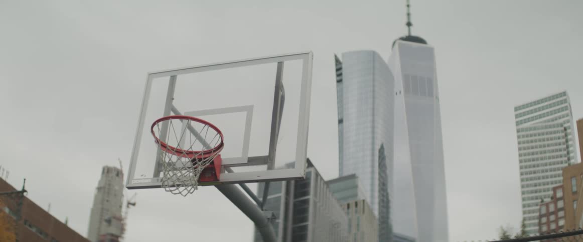 An outdoor basketball court sits near tall skyscrapers in a city