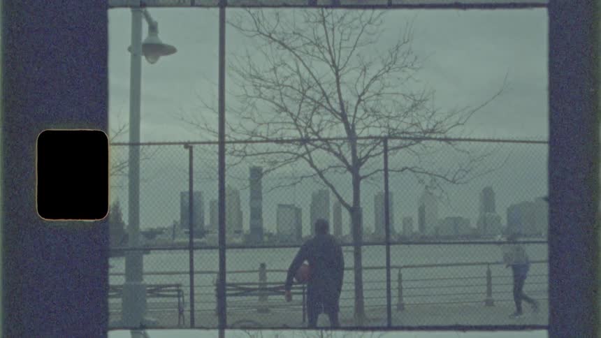 A man stands holding a basketball looking at the city skyline while a jogger goes past