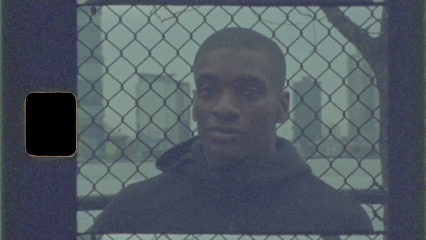 Man stands in front of chain link fence with city skyline across the water