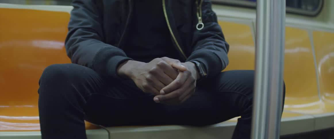 Man sits in a subway car with his hands clasped