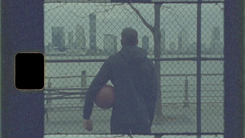 A man stands by the fence with a basketball
