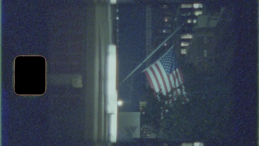 A city street with a large american flag with trees in the foreground and buildings in the background