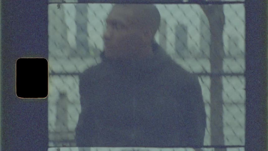 A young black man twirling a basketball around his waist while standing near a fence