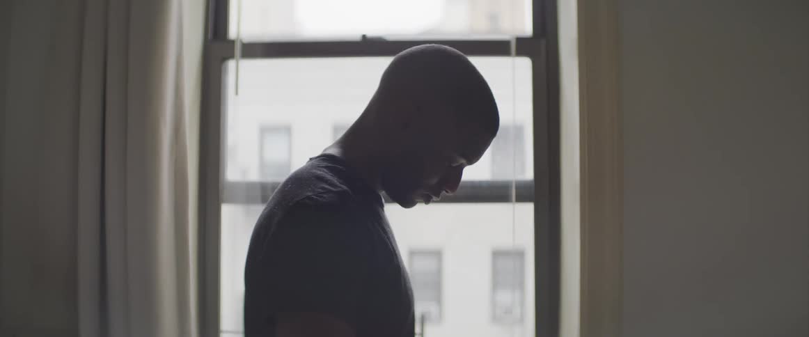 A man stands in a darkened room and stares at the floor