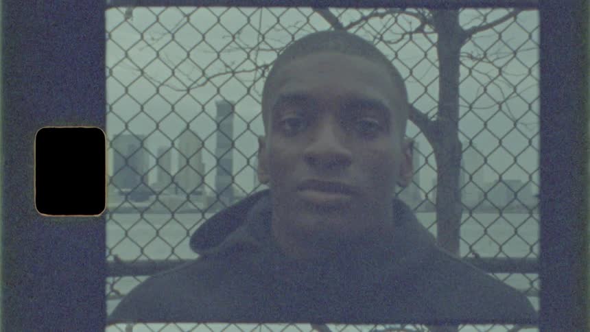 A young man turning to look into the camera while leaning against a fence