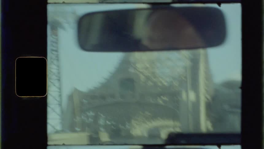 A shot out of the windshield of a shaky car going over a bridge with a person seen in the rearview mirror