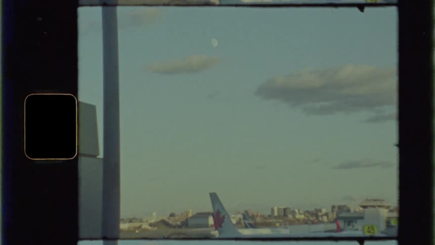 Airliner stands parked next to hanger with buildings on the horizon