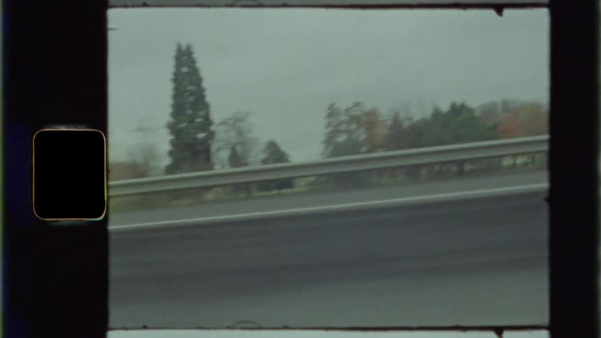 Cars drive along road bordered by trees with fall foliage
