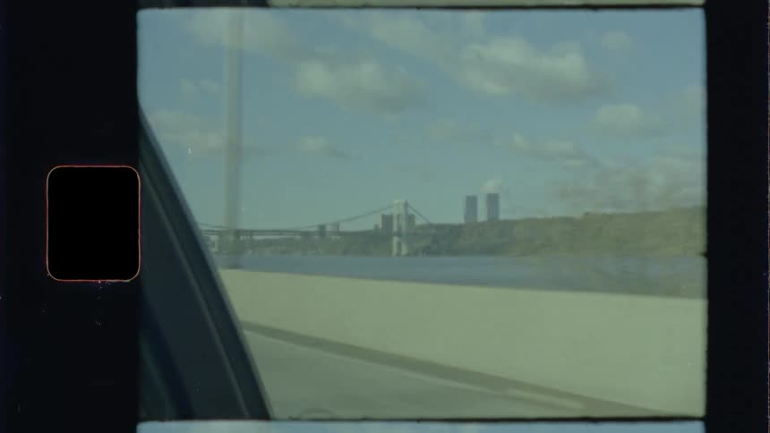 A road next to a river with a bridge and buildings in the background