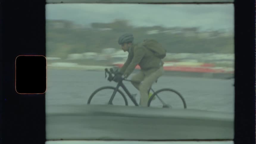 Male wearing a helmet and backpack rides a bicycle along the side of the road next to the river