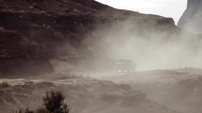 A pickup truck travels on a dusty mountain road