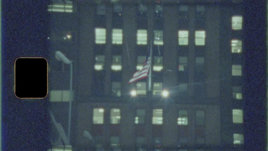 The american flag flies in front of a tall building at night