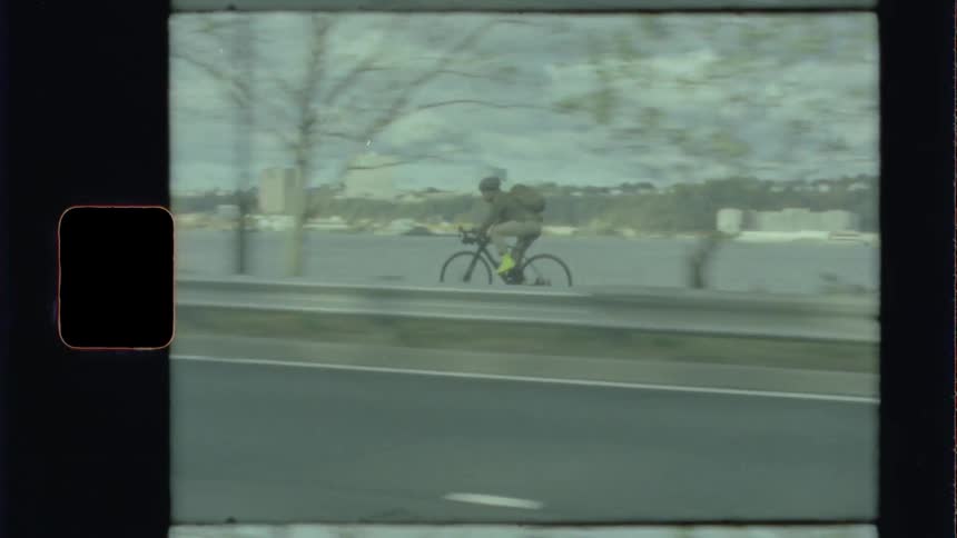 Man with backpack drives bicycle at the side of the road on a city near river