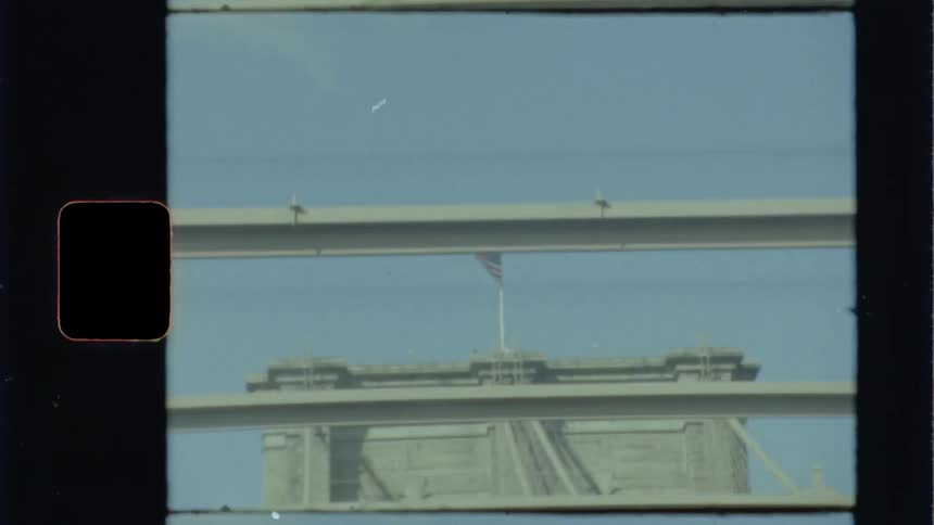 An american flag waving atop the large stone support structure of a bridge