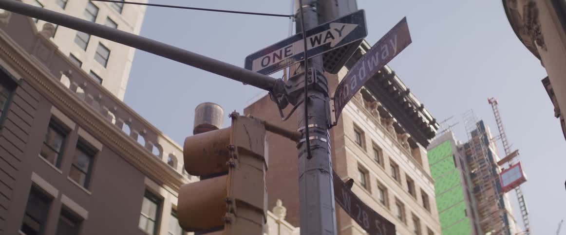 One way sign with an arrow hangs on a post in a city under a blue sky
