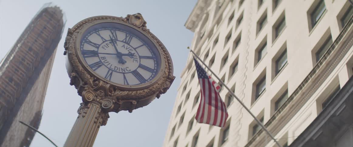 An outdoor clock on a pool near an american flag hanging from a building