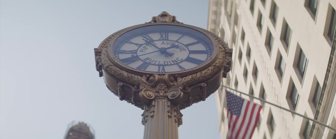 A clock in front of a building with a flag on it