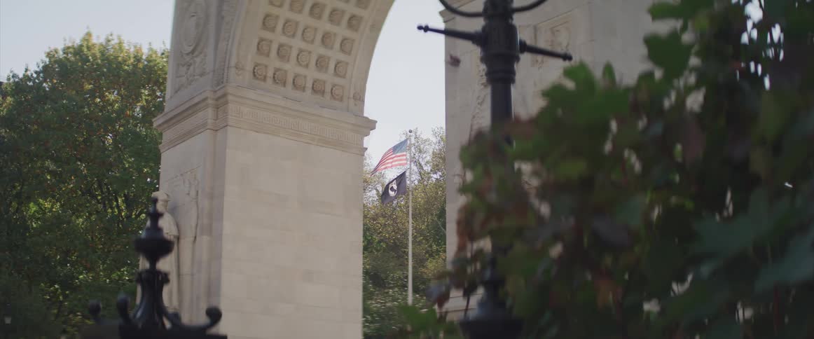 An american flag on a pole waves in the wind behind the arched entrance to a city park