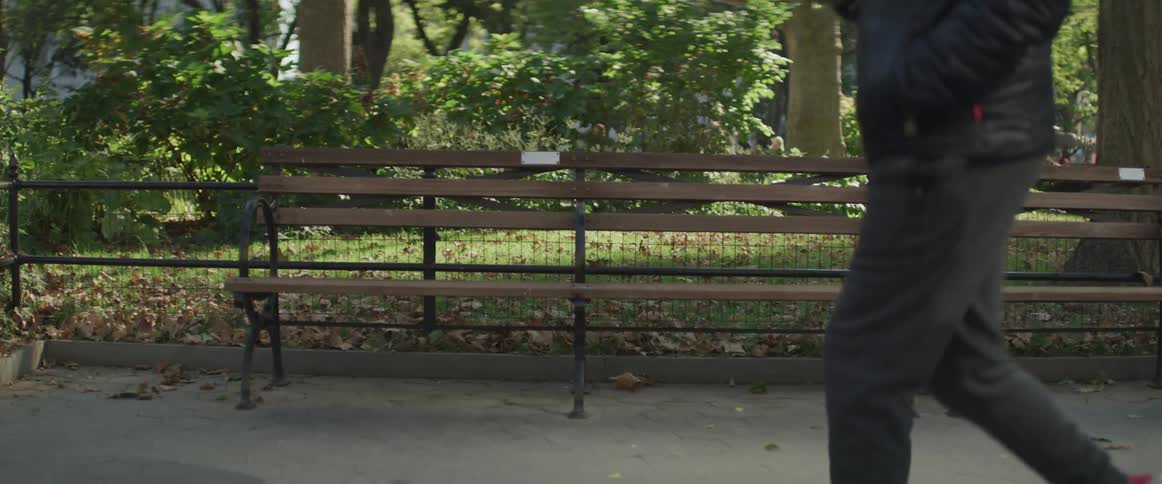 Pedestrians walk past a park bench on a sunny day