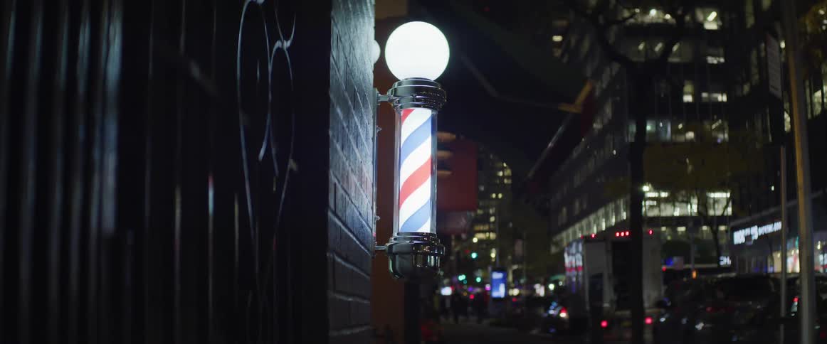 The red white and blue barber pole shine on a city street at night