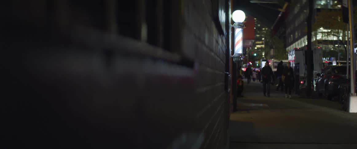 Pedestrians walk down a city sidewalk by a barbershop