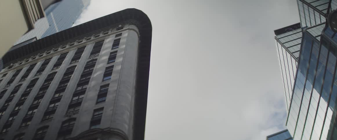 Passing clouds reflect off the side of a mirrored skyscraper in a city