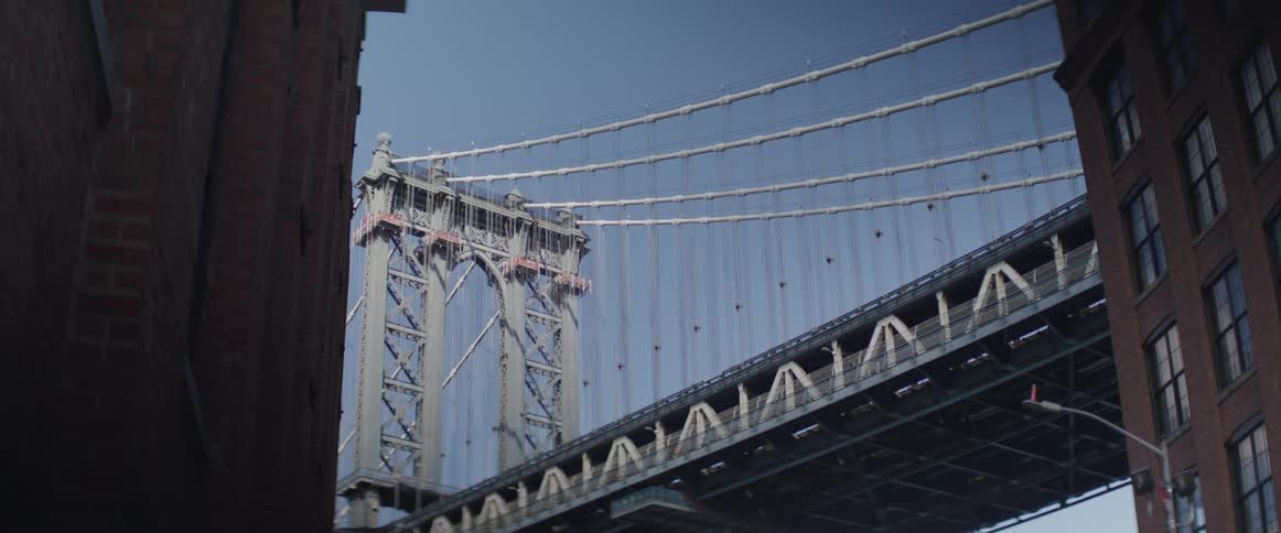 Cars move across a suspension bridge and people walk by in a city