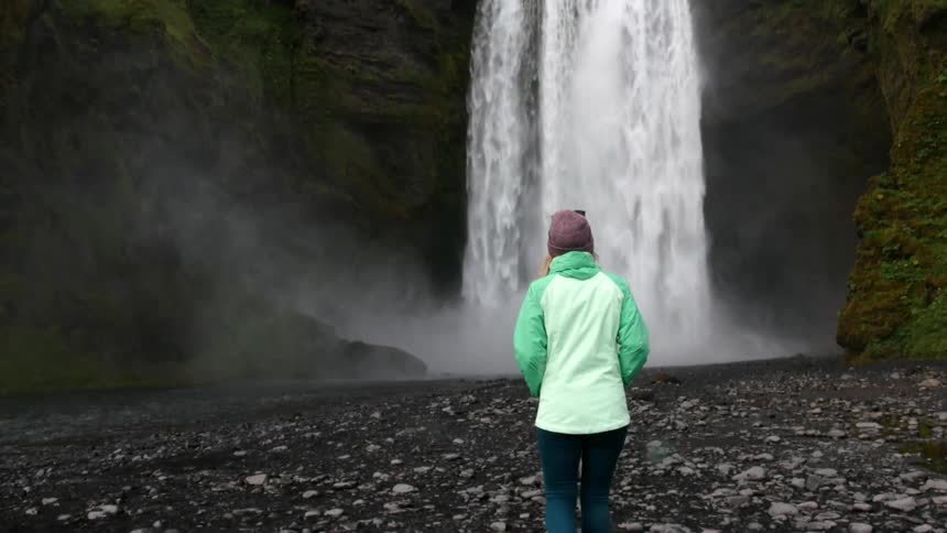 A woman approaches a waterfall in the wilderness