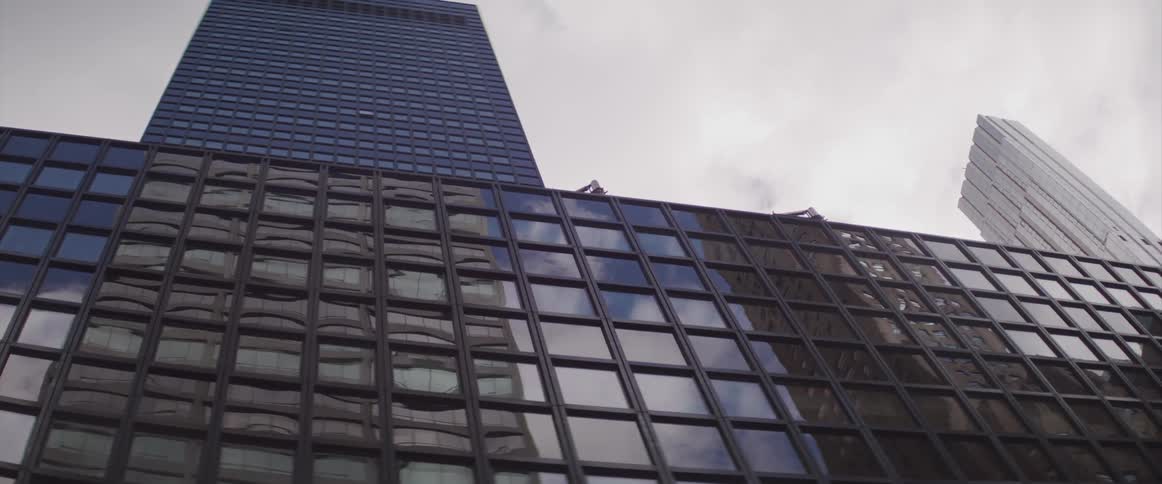 The sky clouds and surrounding buildings are reflected on the glass windows