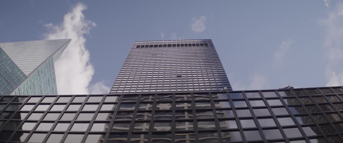 The glass windows on the city building facade reflect the sky and surrounding skyscrapers