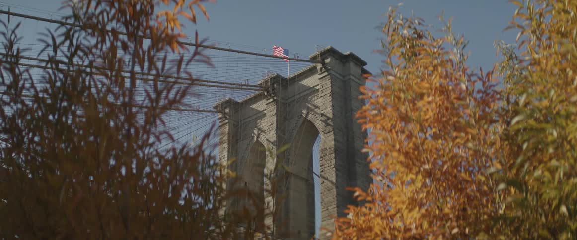 A flag moves in the wind on a post above the arches of a large bridge