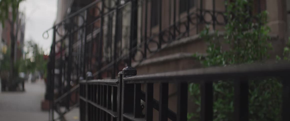 A city sidewalk in front of a brownstone with the sky in the foreground
