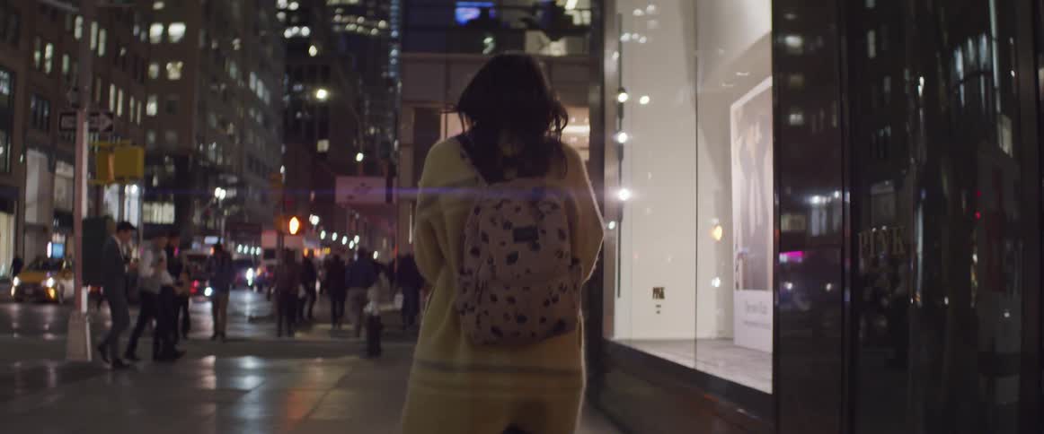 A woman walks a city sidewalk at night