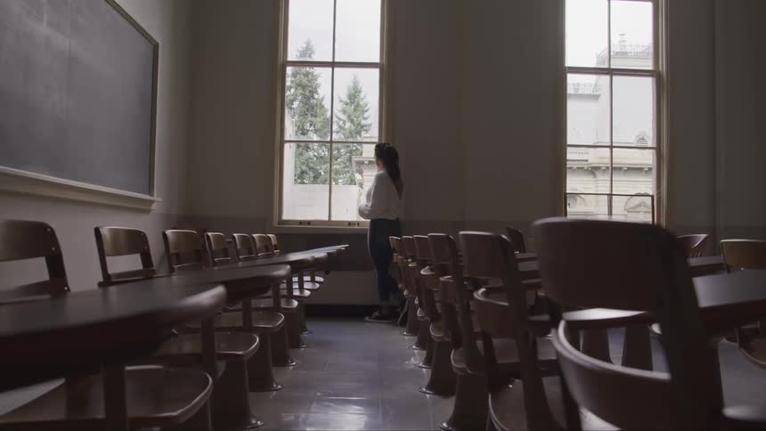 A female stands next to a window in a large classroom