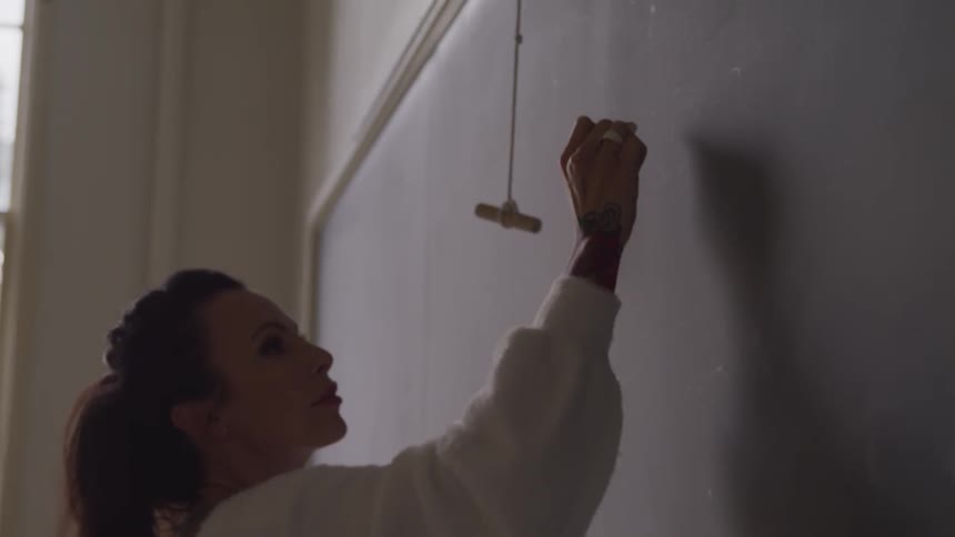Female teacher writes on a chalkboard using chalk in a school classroom