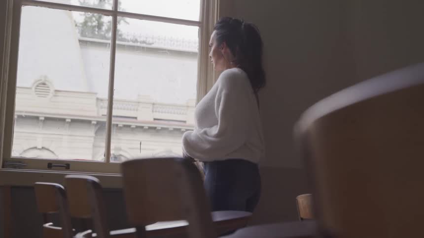 Woman standing indoors in the dark and looking out the window