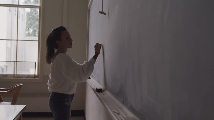 A female teachers writes on a chalkboard