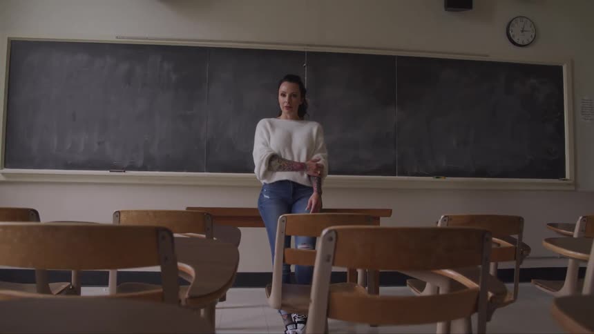 A teacher standing at the front of a classroom on her desk