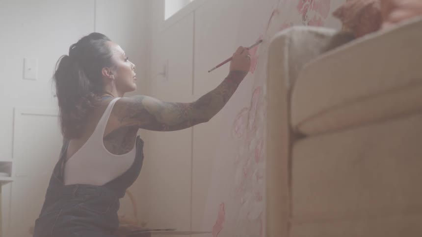 A white woman paints a picture on a wall