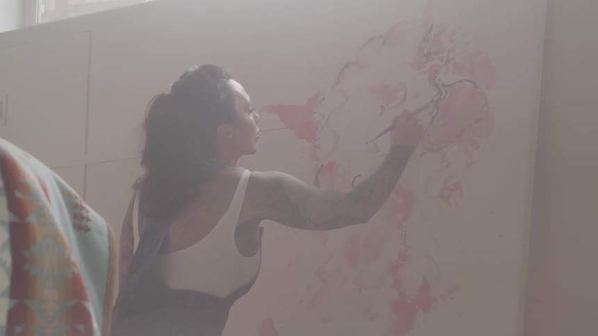 A woman paints a canvas dipping her paintbrush into pink paint