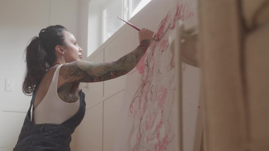 Woman in overalls painting on large canvas in a room