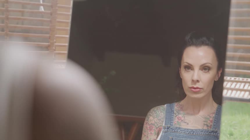 Tattooed woman looks in the mirror in the living room at home