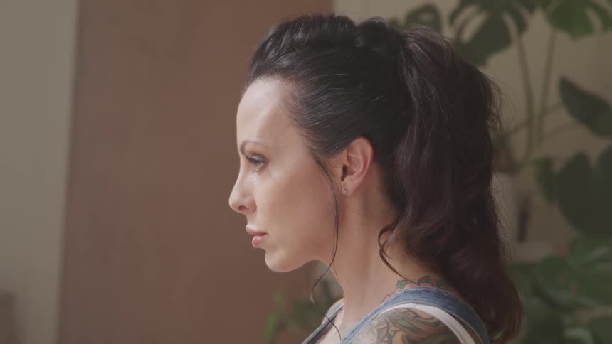A woman with tattoos in a room with plants in the background