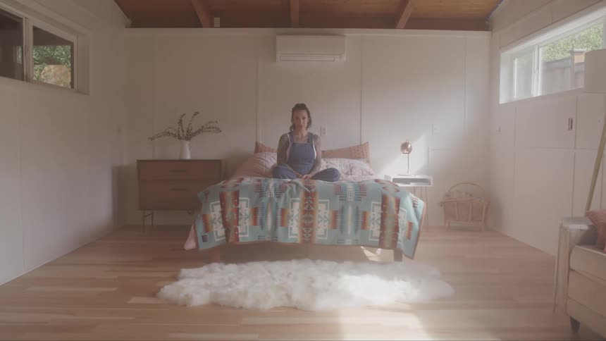 A woman sits on her bed and looks ahead