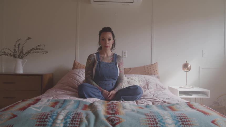 Woman wearing overalls sitting cross legged on a bed