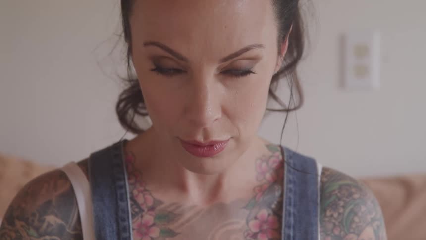 Heavily tattooed white woman raises her head and looks at the camera