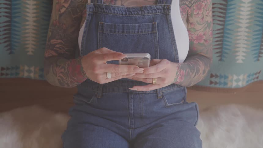 Tattooed woman sitting on a rug uses a smart phone