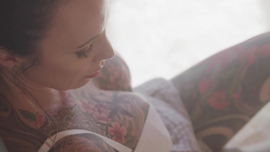 Heavily tattooed woman wearing underwear sits on the couch in the living room