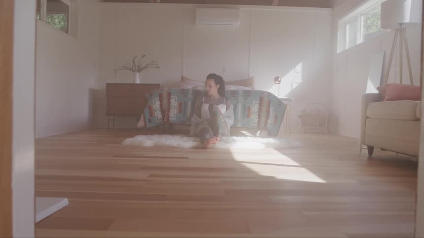 A woman sits on the floor of her bedroom and leans against the bed