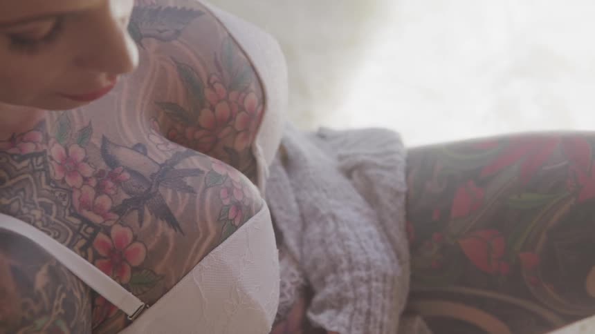 A woman covered in tattoos rests in bed